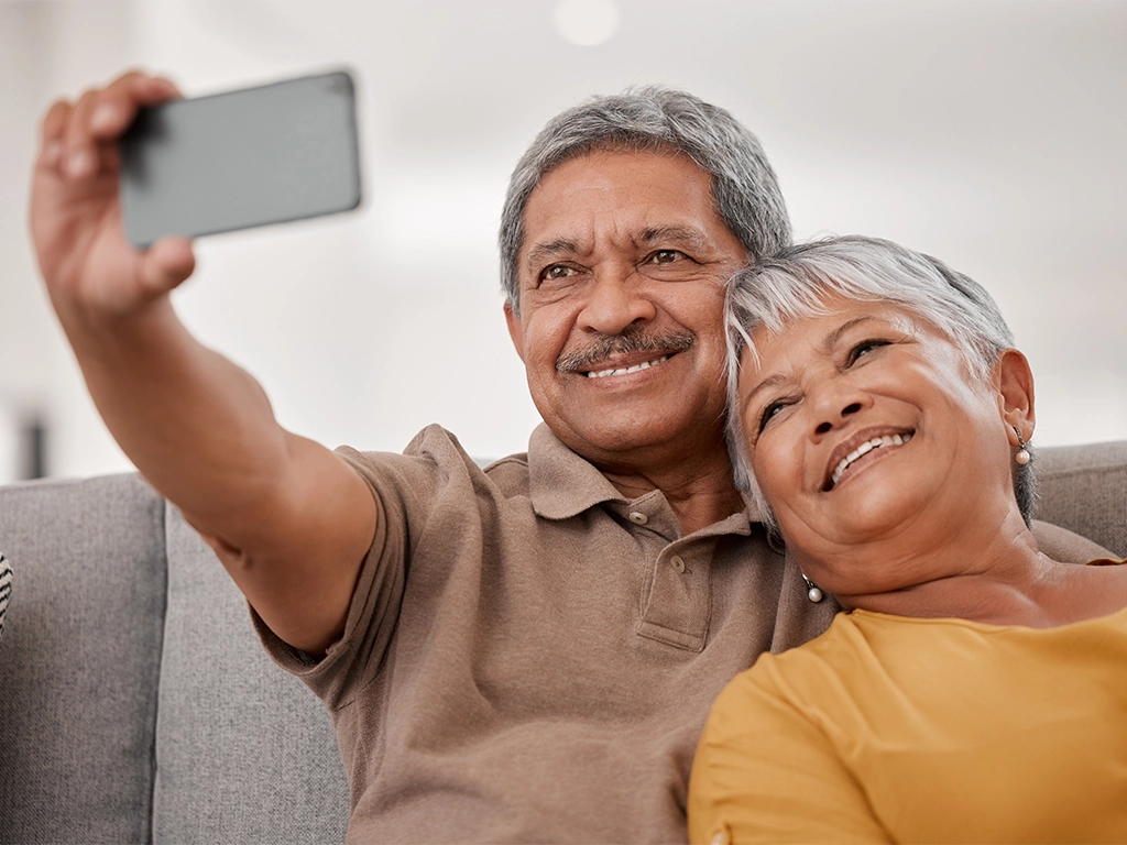 senior couple taking selfie in living room with big smiles
